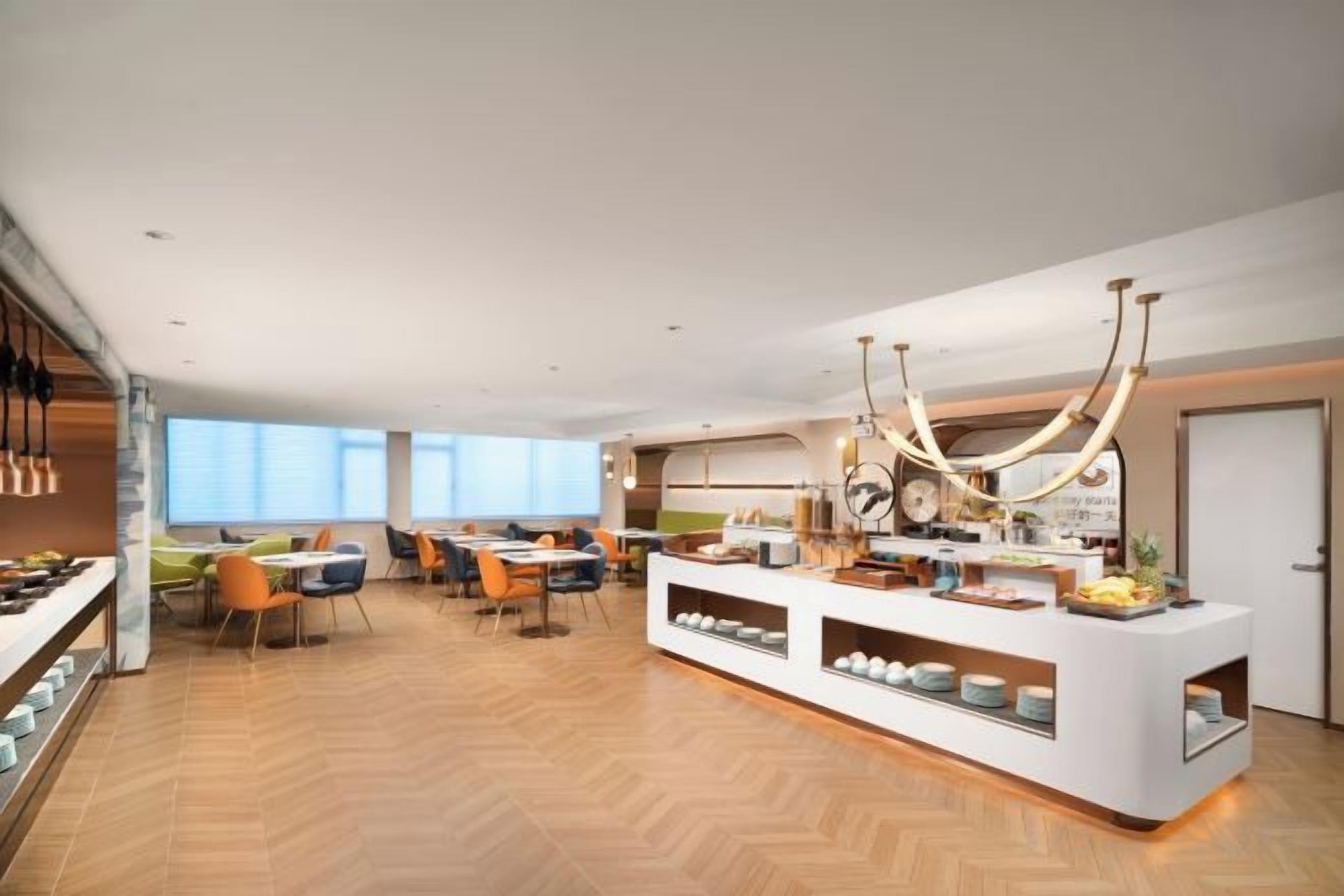 Un hall d’hôtel moderne doté d’un comptoir d’accueil central, de plusieurs espaces de détente et d’une grande fenêtre laissant entrer la lumière naturelle.