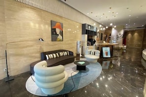 A modern lobby with a sofa, armchairs, a coffee table, and a bookshelf.