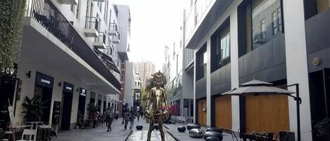 A pedestrian street with shops, outdoor seating, and a statue.