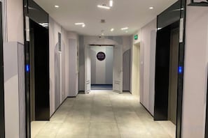 A modern hotel corridor with a straight path, doors on both sides, and a central elevator area.