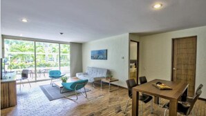 A spacious room with a wooden floor, a dining table with chairs, a sofa, and a large window offering a view of greenery outside. - Hotel Tiburon (Guadalajara)