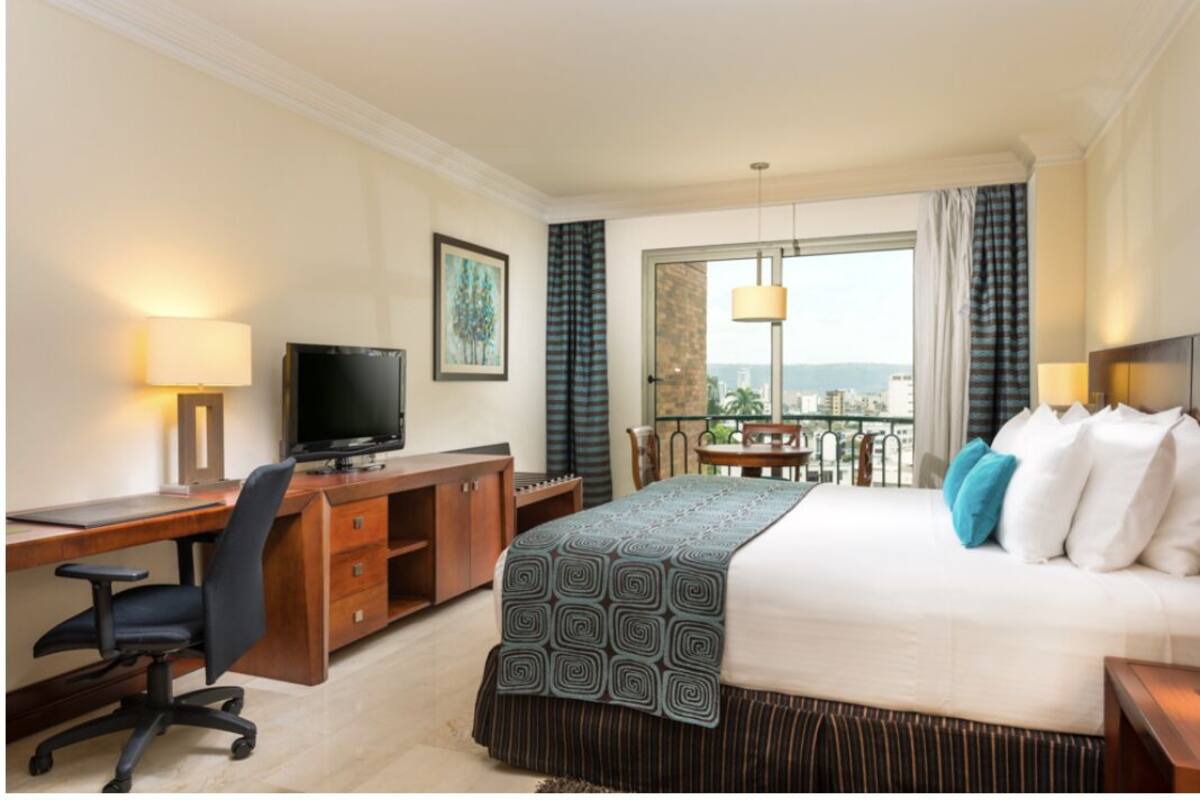 A hotel room with a bed, desk, chair, television, and a balcony with a view.