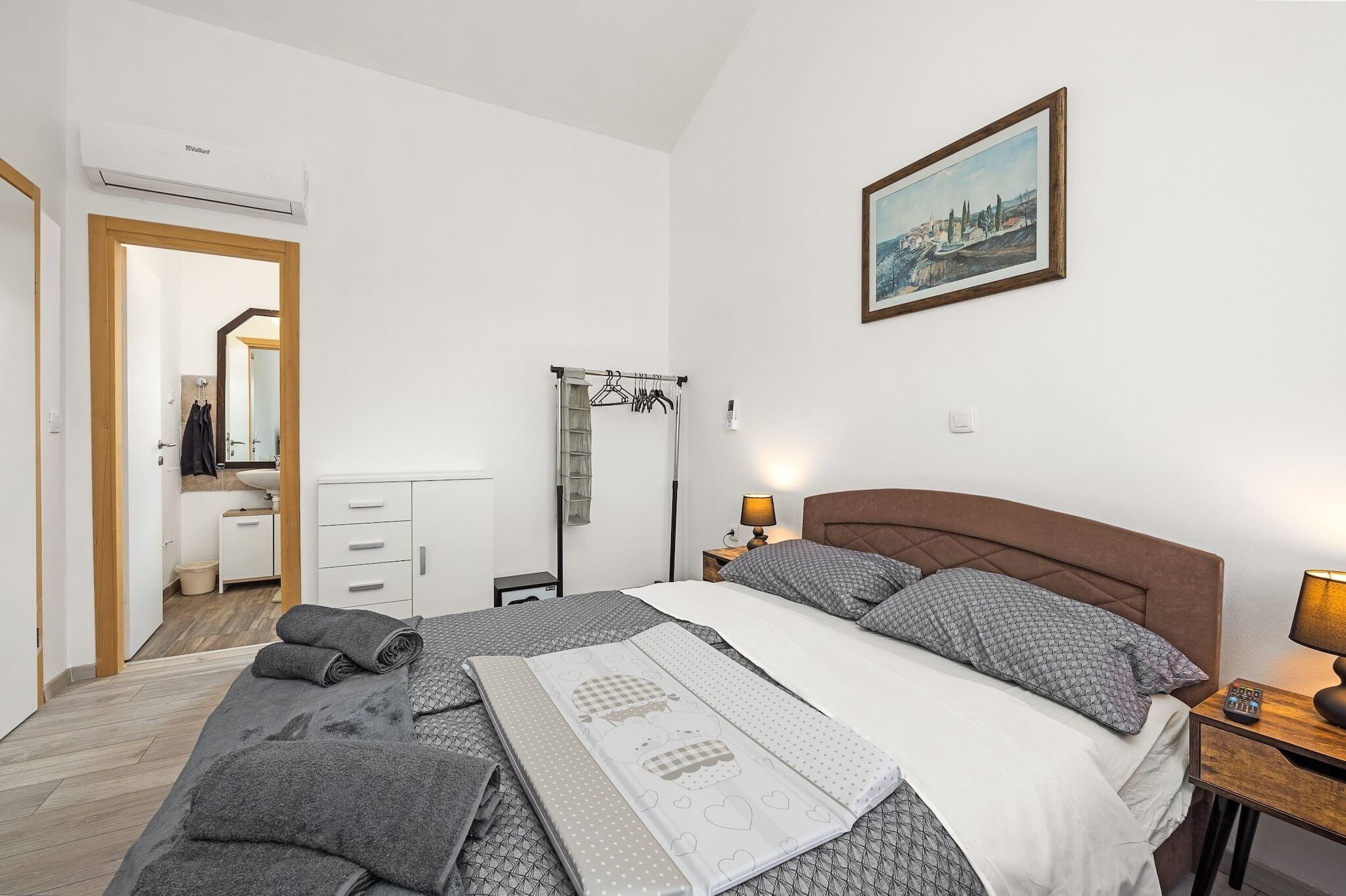 A neatly arranged bedroom with a bed, bedside tables, a lamp, a painting, and a wardrobe.