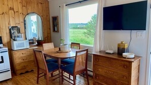 A cozy room with a wooden dining table, chairs, a microwave, a small potted plant, a television, and a dresser. - Cottage #6 - 1 bedroom - pet friendly! (French River)