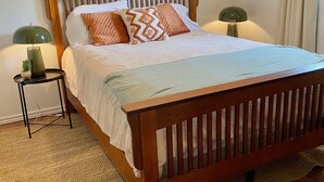 A neatly made bed with a wooden headboard, two bedside lamps, and a woven rug on a wooden floor. - Cottage #6 - 1 bedroom - pet friendly! (French River)