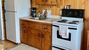 A kitchen with wooden cabinets, a white refrigerator, a stove, and a coffee maker. - Cottage #6 - 1 bedroom - pet friendly! (French River)