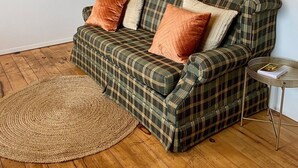 A plaid sofa with cushions, a woven rug, and a small side table with a book. - Cottage #6 - 1 bedroom - pet friendly! (French River)