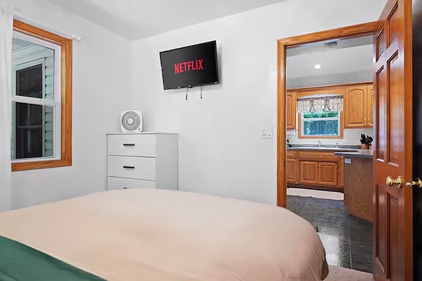 A bedroom with a bed, a TV mounted on the wall, and a window with blinds.