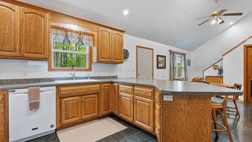 A kitchen with wooden cabinets, a built-in dishwasher, a large island, and a ceiling fan.