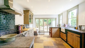 Een moderne keuken met een stenen tegelvloer, houten kastjes en een groot raam dat zorgt voor natuurlijk licht.
