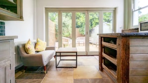 Een moderne keuken met een inbouwoven, een eethoek met een bank en stoelen, en een schuifdeur van glas die leidt naar een terras met buitenmeubilair.