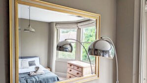 Een slaapkamer met een grote spiegel, een bed met een blauwe deken, een dressoir en een radiator.