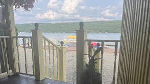 Terraza de madera con barandilla, una planta en maceta y vista a un lago con barcos y sombrillas.