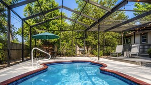 A swimming pool with a glass enclosure, surrounded by a patio area with chairs and a table. - Cozy Clearwater Pool Home Near Beaches! (Clearwater)