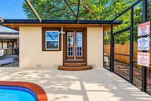 A pool area with a covered patio, a pool with a red tile edge, and multiple warning signs including 'No Diving' and 'No Lifeguard on Duty'. - Cozy Clearwater Pool Home Near Beaches! (Clearwater)