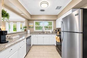 Cocina moderna con armarios blancos, refrigerador de acero inoxidable y cafetera.
