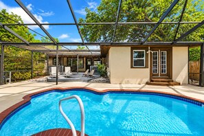 A swimming pool with a clear blue water, surrounded by a covered patio area with chairs and a wooden deck. - Cozy Clearwater Pool Home Near Beaches! (Clearwater)