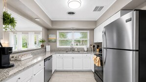 A modern kitchen with white cabinets, a stainless steel refrigerator, a coffee maker, and a window with blinds. - Cozy Clearwater Pool Home Near Beaches! (Clearwater)