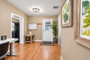 A hallway with a wooden floor, a door with a calendar, a plant, and a framed picture on the wall. - Cozy Clearwater Pool Home Near Beaches! (Clearwater)