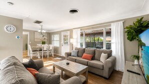 A living room with a sofa, coffee table, and a TV. There is a dining area with chairs and a table. - Cozy Clearwater Pool Home Near Beaches! (Clearwater)