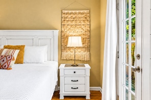 Un dormitorio con cama, mesita de noche, lámpara y ventana con cortinas.