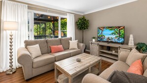 A living room with a sofa, coffee table, TV, and a view of a garden. - Cozy Clearwater Pool Home Near Beaches! (Clearwater)