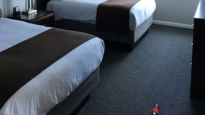 A hotel room with two beds, a ceiling fan, a window with curtains, and a bedside table with a lamp.