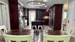 A dining area with a wooden table and white chairs, a chandelier, and dark wooden cabinets. - Vacation Farmhouse (Lufkin)