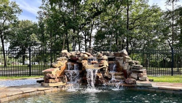 A rock waterfall feature in a park with a clear pool at the base. - Vacation Farmhouse (Lufkin)