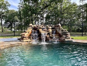 A rock waterfall feature in a park with a clear pool at the base. - Vacation Farmhouse (Lufkin)