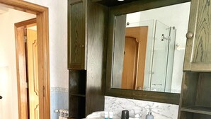 A bathroom with a marble sink, wooden cabinetry, and a large mirror. - R. Principal 25 (Torres Vedras)