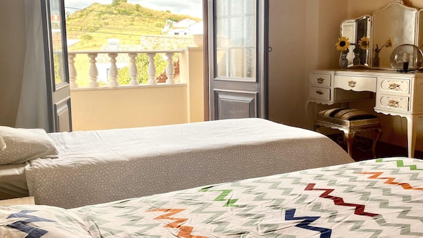 A bedroom with two beds, a dresser, and a balcony with a view of a hill. - R. Principal 25 (Torres Vedras)