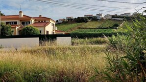 A residential area with houses on a hillside, power lines overhead, and a grassy foreground. - R. Principal 25 (Torres Vedras)