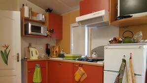 A compact kitchen with red cabinets, a microwave, a kettle, a stove, and a refrigerator.