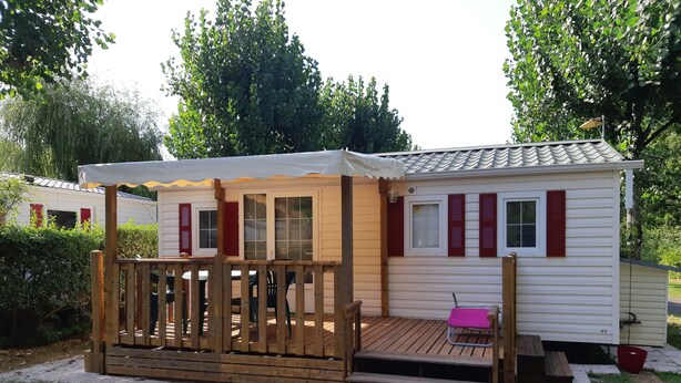 A small, single-story mobile home with a wooden deck and a covered porch.