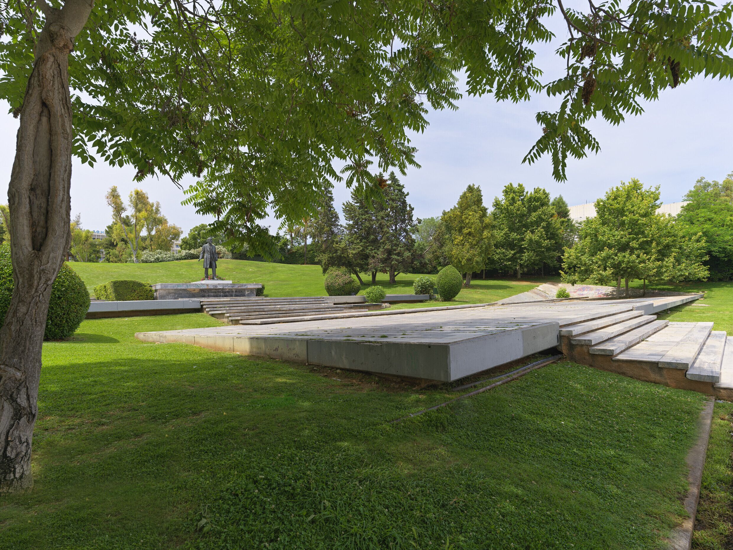 Un parc avec une statue, une pelouse et un chemin piétonnier dallé.