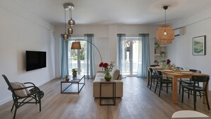 Un salon moderne doté d’un téléviseur à écran plat, d’un canapé, d’une table basse et d’un coin repas avec une table et des chaises en bois.