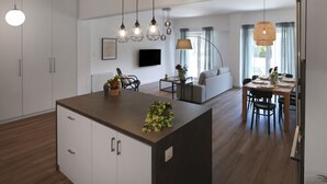 Une cuisine moderne avec un îlot central, un coin repas avec une table dressée pour deux personnes, et un espace de vie avec un canapé et un téléviseur.