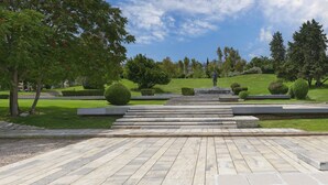 Un parc agrémenté d’une statue, de marches en pierre, ainsi que d’une pelouse et d’arbres bien entretenus.