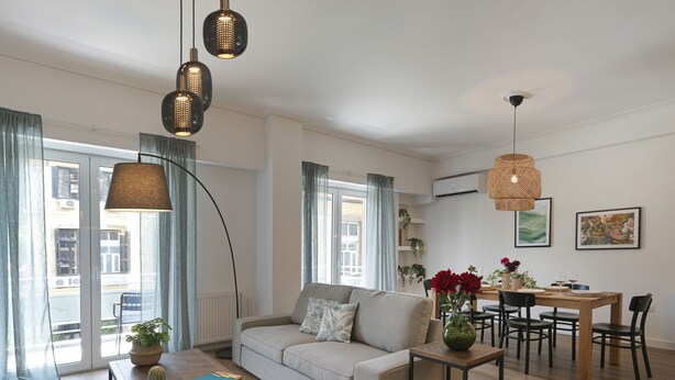 Un salon moderne comprenant un canapé, une table basse, une table à manger et des chaises. On y trouve également des plantes, un vase avec des fleurs et des œuvres d’art accrochées aux murs.