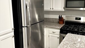 A kitchen with white cabinets, a stainless steel refrigerator, a microwave, and a stove.