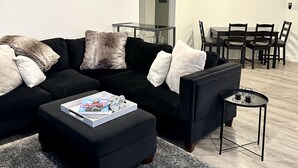 A modern living room with a sectional sofa, a coffee table, and a dining area with a table and chairs.