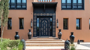 A building with a large, ornate black door, multiple windows, and steps leading to the entrance. - Villa Chems (Marrakech)