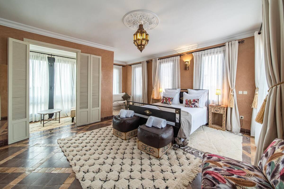 Un dormitorio amplio con una cama grande, una zona de estar con sofá y sillón, y un tapete decorativo.