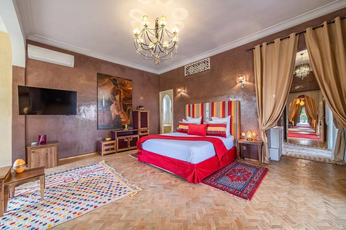 Un dormitorio amplio con una cama grande, una araña, un televisor de pantalla plana y vistas a un patio.