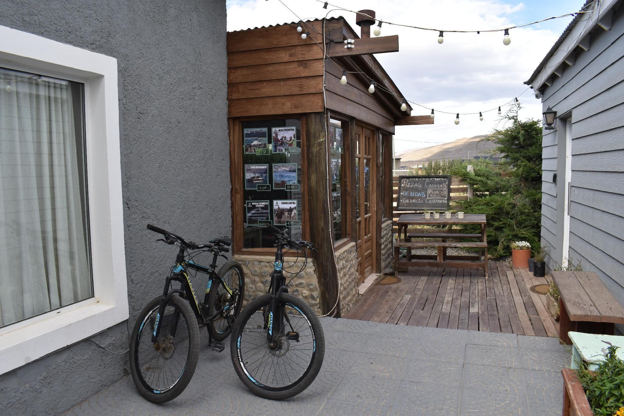 Una terraza de madera con dos bicicletas estacionadas, un menú en una pizarra y un edificio de madera con techo inclinado.