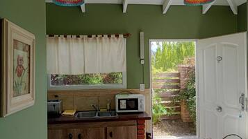 A kitchen with a microwave, sink, and wooden cabinets. There is a window with a curtain, and a door leading outside.