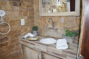 A bathroom with a stone wall, a white sink, a mirror, and a towel on the counter. - Tierra de Glaciares Aparts Cabañas (El Calafate)
