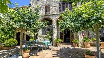 Un edificio de piedra con patio, mesas al aire libre y macetas con plantas.