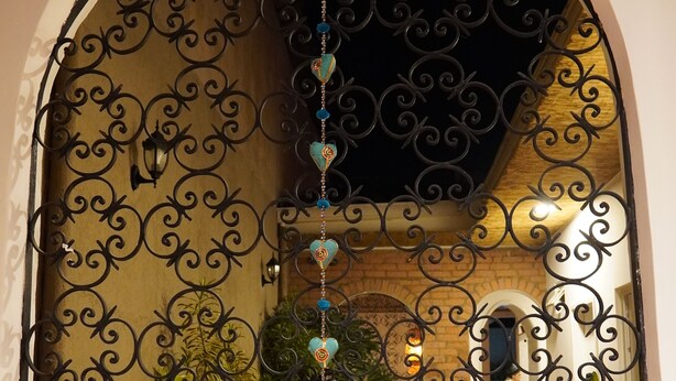 Una finestra ad arco con elaborate decorazioni in metallo nero, vasi in terracotta con diverse piante e un ornamento decorativo appeso.